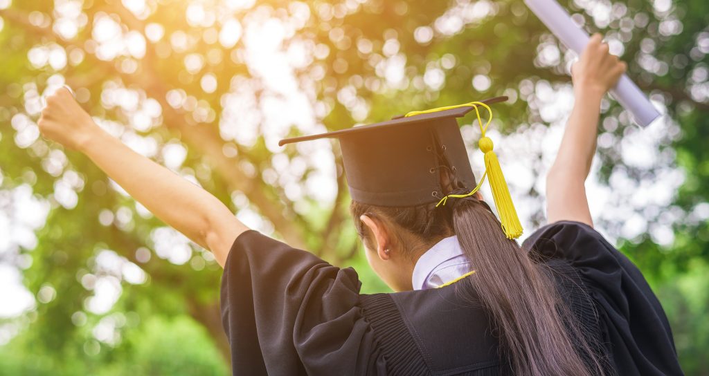 Female high school graduate celebrating in cap and gown.