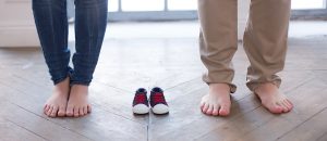 A couple that's expecting a baby standing with a pair of baby shoes between them